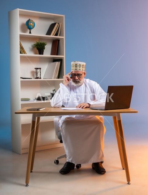 Using advanced modern technologies, portrait of an elderly Arab Gulf Omani man wearing a kemeh and a dishdasha, putting his hand on his head with expressions of thinking and remembering, trying to find a solution to a problem, expressions of absent-mindedness, concentration and contemplation, colored background
