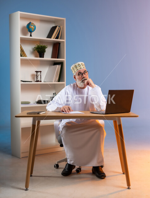 Looking at something above, gestures of remembrance and distraction, portrait of an elderly Gulf Omani man wearing a dishdasha, traditional Omani kummah and glasses, putting his hand on his chin with expressions of remembering something, using modern advanced technologies, colorful background