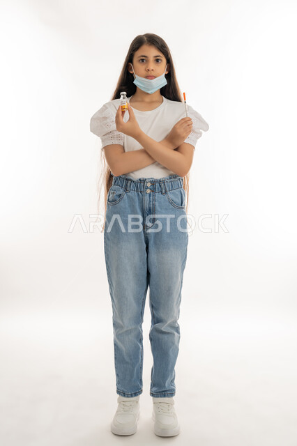 تجنب إنتشار العدوى، التطعيم الآمن لكوفيد19، اتباع اجراءات وزارة الصحة الوقائية، مفهوم الوعي الصحي، بورتريه لفتاة عربية خليجية إماراتية ترتدي الكمامة تحمل بيدها ابرة وجرعة من لقاح فايروس كورونا، الحماية من الأمراض والحفاظ على السلامة، الجسم الكامل بالطول، خلفية بيضاء