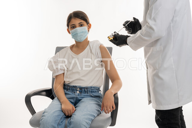طبيب يرتدي المعطف الأبيض والقفازات يجهز جرعة لقاح كوفيد-19، بورتريه مقرب لفتاة عربية خليجية اماراتية ترتدي الكمامة تستعد لتلقي اللقاح، اتباع إجراءات وزارة الصحة الوقائية، إتاحة التطعيم ضد فايروس كورونا، الحماية من الأمراض والمحافظة على السلامة، تجنب انتشار العدوى، خلفية بيضاء
