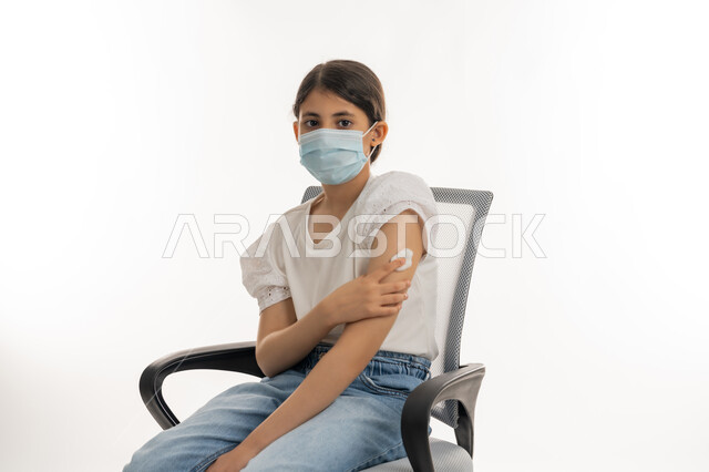 التطعيم الآمن لكوفيد19، تجنب إنتشار العدوى، الحماية من الأمراض والحفاظ على السلامة، اتباع اجراءات وزارة الصحة الوقائية، مفهوم الوعي الصحي، بورتريه لفتاة عربية خليجية إماراتية ترتدي الكمامة تضع يدها مكان الحقن، خلفية بيضاء