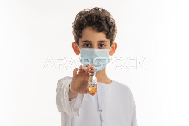 اتباع اجراءات وزارة الصحة الوقائية، تجنب إنتشار العدوى، مفهوم الوعي الصحي، الحماية من الأمراض والحفاظ على السلامة، التطعيم الآمن لكوفيد19، بورتريه لولد عربي خليجي إماراتي يرتدي الكندورة والكمامة يحمل بيده جرعة من لقاح فايروس كورونا، خلفية بيضاء