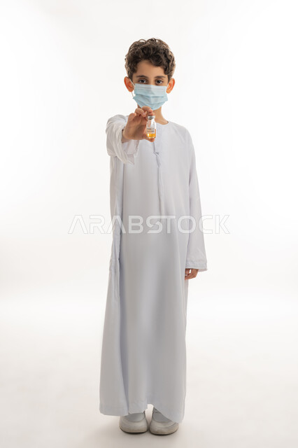 التطعيم الآمن لكوفيد19، اتباع اجراءات وزارة الصحة الوقائية، تجنب إنتشار العدوى، مفهوم الوعي الصحي، الحماية من الأمراض والحفاظ على السلامة، بورتريه لولد عربي خليجي إماراتي يرتدي الكندورة والكمامة يحمل بيده جرعة من لقاح فايروس كورونا، الجسم الكامل بالطول، خلفية بيضاء