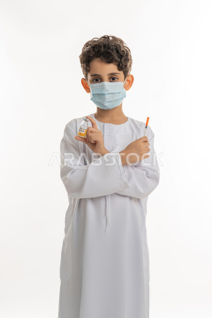تجنب إنتشار العدوى، الحماية من الأمراض والحفاظ على السلامة، مفهوم الوعي الصحي، بورتريه لولد عربية خليجي إماراتي يرتدي الكندورة  والكمامة يحمل بيده ابرة وجرعة من لقاح فايروس كورونا، اتباع اجراءات الوقاية، التطعيم الأمن لكوفيد19 ، خلفية بيضاء