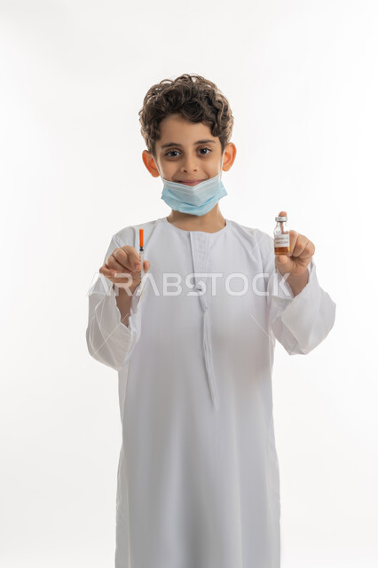 الحماية من الأمراض والحفاظ على السلامة، تجنب إنتشار العدوى، مفهوم الوعي الصحي، بورتريه لولد عربية خليجي إماراتي يرتدي الكندورة  الكمامة يحمل بيده ابرة وجرعة من لقاح فايروس كورونا، اتباع اجراءات الوقاية، التطعيم الأمن لكوفيد19، خلفية بيضاء
