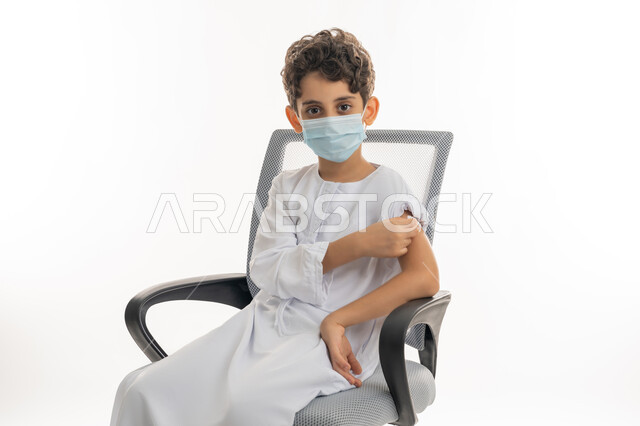 تجنب إنتشار العدوى، الحماية من الأمراض والحفاظ على السلامة، مفهوم الوعي الصحي، بورتريه لولد عربية خليجي إماراتي يرتدي الكندورة  والكمامة يجلس على الكرسي، اتباع اجراءات الوقاية، التطعيم الأمن لكوفيد19 ، خلفية بيضاء