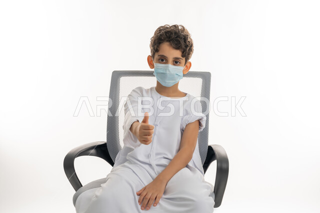 الحماية من الأمراض والحفاظ على السلامة، تجنب إنتشار العدوى، مفهوم الوعي الصحي، بورتريه لولد عربية خليجي إماراتي يرتدي الكندورة  والكمامة يرفع اصبع الإبهام للأعلى بتعابير الاعجاب والقبول، اتباع اجراءات الوقاية، التطعيم الأمن لكوفيد19 ، خلفية بيضاء