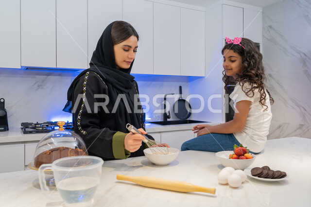 قضاء أوقات ممتعه مع الابنه في المطبخ، اعداد وتحضير الحلويات الطازجه في المنزل, الوقوف أمام طاولة المطبخ, مقادير صنع الكعك، ام عربيه خليجية امارتية محجبه تقف مع ابنتها يقومان بتحضير الطعام، عائلة سعودية سعيدة، المشاركة بالأعمال المنزلية، تعلم وصفات جديدة