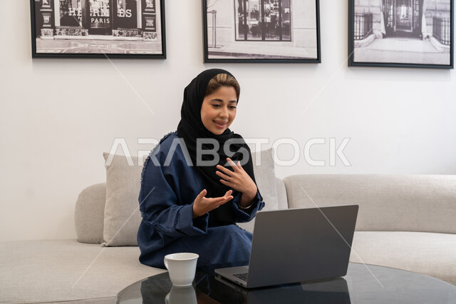 ايماءات التركيز والاندماج، دمج التكنولوجيا بالعمل، مهن ووظائف سعودية نسائية، ادارة الأعمال عن بعد، إمرأة عربية خليجية سعودية ترتدي العباءة والحجاب تستخدم الحاسوب المحمول، إنجاز المهام في المنزل، سيدة اماراتية تقوم باستخدام الأجهزة والتقنيات الحديثة والمتطورة