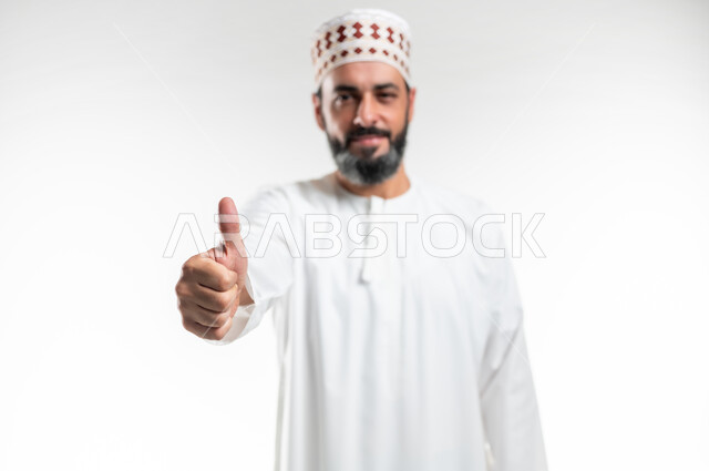 الموافقة على أمر معين، ايماءات الرضا والسرور والسعادة، حركات الاعجاب والقبول, بورتريه مقرب لرجل عربي خليجي عماني مبتسم يرتدي الدشداشة و الكمه ينظر الى الكاميرا يرفع اصبعه الإبهام للأعلى بتعابير علامة الجودة, خلفية بيضاء