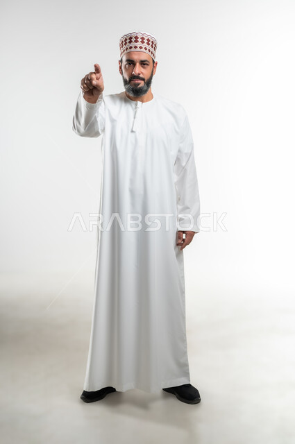 التوبيخ و الإتهام وإلقاء اللوم، طلب التوقف عن فعل الأخطاء، الشعور بالإنزعاج والرغبة بالإنتقام، بورتريه لرجل عربي خليجي عماني يرتدي الدشداشة و الكمه يرفع اصبع السبابه الى الأمام لتحديد شخص ما ( أنت )، صورة الجسم بالطول الكامل، خلفية بيضاء
