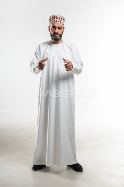 Determining volume and mass, using hands to measure something, portrait of an Arab Gulf Omani man wearing a dishdasha and a kummah standing straight and raising his hands in gestures of carrying something, concept of presenting and displaying a certain item, full length body image, white background