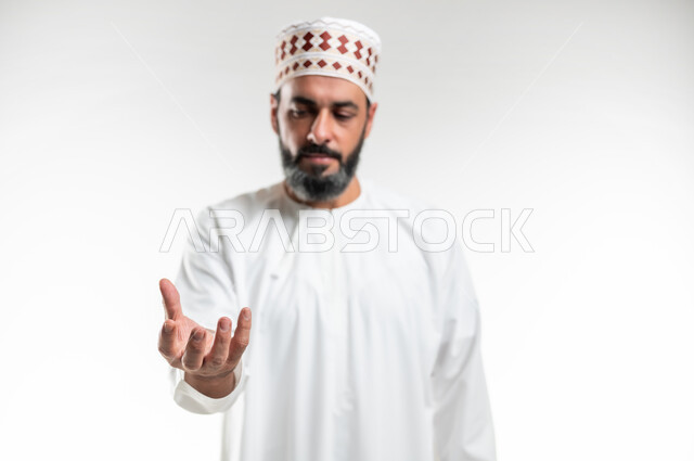 إمساك وإحتواء عنصر معين، حركات وإشارات يدين تدل على رفع الأشياء، بورتريه مقرب لرجل عربي خليجي عماني يرتدي الدشداشة العمانية والكمه يقف باستقامة ويرفع يده الى الأعلى بتعابير حمل شيء ما، خلفية بيضاء