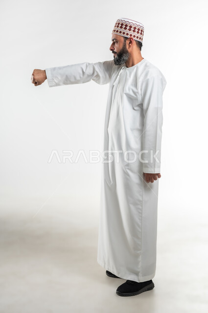 ممارسة رياضة الدفاع عن النفس، زيادة قدرة العضلات على التحمل، إتقان فنون الملاكمة، بورتريه لرجل عربي خليجي عماني يرتدي الدشداشة التقليدية والكمة يرفع قبضات يده بإيماءات القوة، تعزيز صحة العظام والمفاصل، الطول الكامل للجسم، خلفية بيضاء