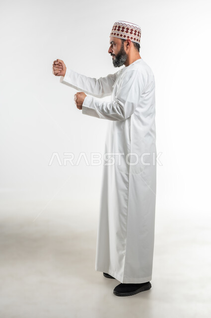 زيادة قدرة العضلات على التحمل، إتقان فنون الملاكمة، بورتريه لرجل عربي خليجي عماني يرتدي الدشداشة التقليدية والكمة يرفع قبضات يديه بإيماءات القوة، ممارسة رياضة الدفاع عن النفس، تعزيز صحة العظام والمفاصل، الطول الكامل للجسم، خلفية بيضاء