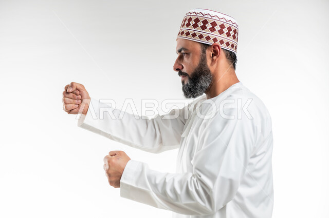 إتقان فنون الملاكمة، زيادة قدرة العضلات على التحمل، بورتريه مقرب لرجل عربي خليجي عماني يرتدي الدشداشة التقليدية والكمة يرفع قبضات يديه بإيماءات القوة، ممارسة رياضة الدفاع عن النفس، تعزيز صحة العظام والمفاصل، خلفية بيضاء