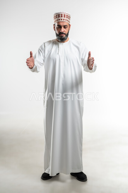 Measuring and determining the size of objects, the concept of presenting and displaying a certain item, a portrait of an Arab Gulf Omani man wearing the traditional dishdasha and the kummah raising his hands with gestures of carrying something, signs and hand movements indicating lifting and holding, full body length, white background
