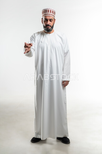 ايماءات يد لرمي و اطلاق عنصر معين، الرغبة بالتخلص وإبعاد شيء ما, بورتريه لرجل عربي خليجي عماني يرتدي الدشداشة العمانية والكمه يرفع يده نحو الأمام بحركات أصابع تدل على اتقان لعبة ما، صورة الجسم بالطول الكامل، خلفية بيضاء