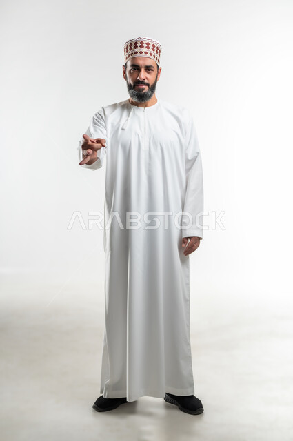 الرغبة بالتخلص وإبعاد شيء ما, حركة يد لرمي و اطلاق عنصر معين، بورتريه لرجل عربي خليجي عماني يرتدي الدشداشة العمانية والكمه يرفع يده نحو الأمام بحركات أصابع تدل على اتقان لعبة ما، صورة الجسم بالطول الكامل، خلفية بيضاء