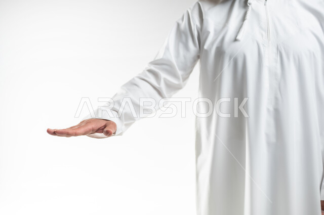 تحديد طول وإرتفاع شيء ما، بورتريه مقرب ليد رجل عربي خليجي عماني يرتدي الدشداشة التقليدية العمانية يمد راحة كفه نحو الأسفل بايماءات وجود عنصر معين، تعابير واشارات يدين تدل على قياس مسافة ما، خلفية بيضاء