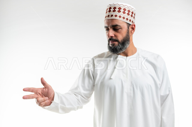 الاشارة إلى شيء ما، اشارات تحدد هذا المكان (هنا)، تعابير التحديد والتأكيد, بورتريه مقرب لرجل عربي خليجي عماني يرتدي الدشداشة والكمه يقف باستقامة و يشير بثلاث أصابع للإختيار، خلفية بيضاء