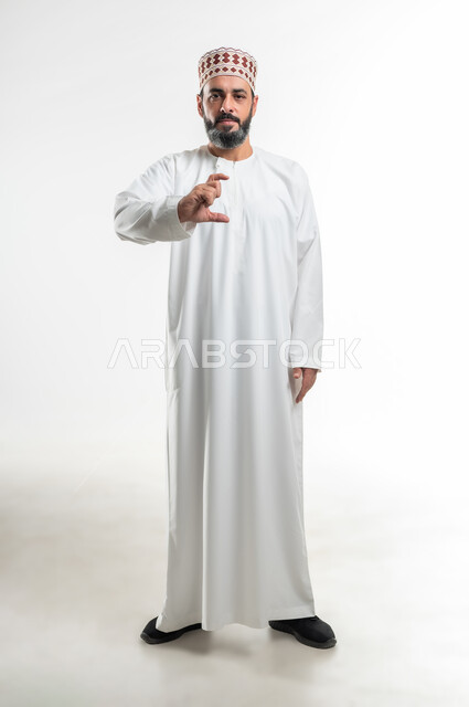حركات وإشارات يدين تدل على الإمساك بشيء ما، تحديد كمية أو مسافة معينة، بورتريه لرجل عربي خليجي عماني يرتدي الدشداشة والكمة يرفع يده للأعلى بإيماءات رفع و حمل عنصر محدد، صورة الجسم بالطول الكامل، خلفية بيضاء