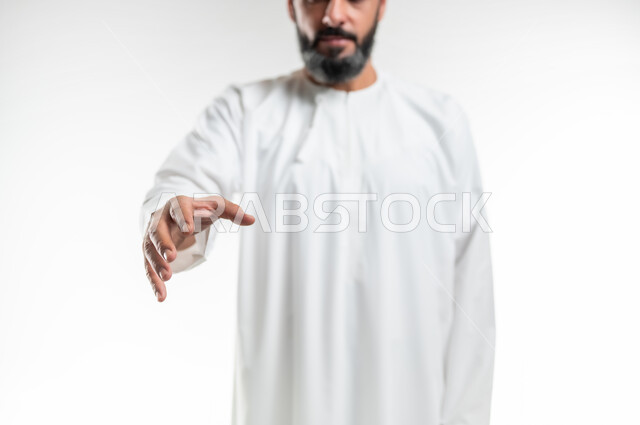 محاولة الإمساك بشيء ما، مفهوم الترحيب و السلام و إلقاء التحية، بورتريه مقرب لرجل عربي خليجي عماني يرتدي الدشداشة يقوم بمد يده نحو الأمام لإلتقاط عنصر ما، حركات يدين تدل على المصافحة، خلفية بيضاء