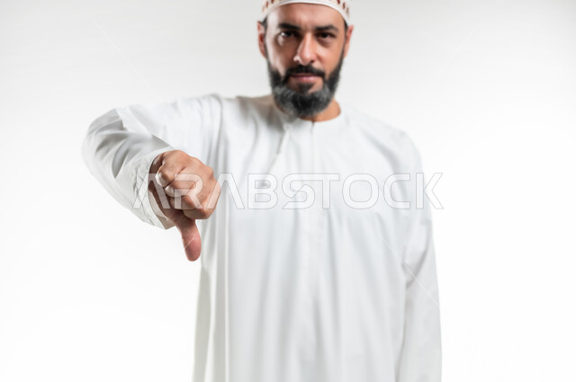حركات يدين تدل على الرفض وعدم القبول والفشل، بورتريه مقرب لرجل عربي خليجي عماني يرتدي الدشداشة و الكمه يشير بإصبعه الابهام الى الأسفل بإيماءات عدم الاعجاب والتقييم السلبي، الشعور بالانزعاج من شيء ما، خلفية بيضاء