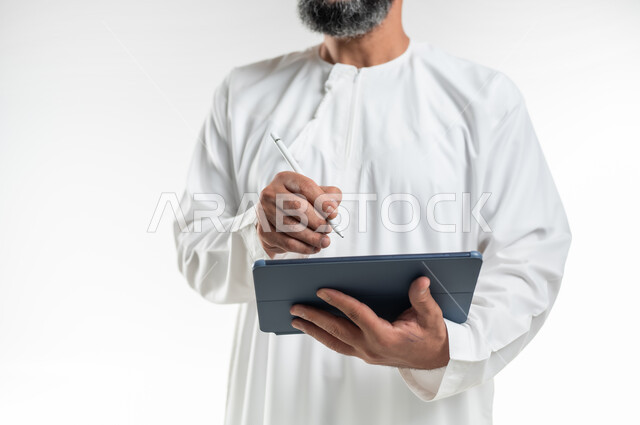Tablet applications and programs, chatting with family and friends, using technology and modern techniques, close-up portrait of an Arab Gulf Omani man wearing a dishdasha writing on a tablet, browsing social media programs, white background