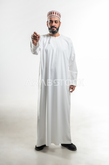 Recording and taking notes, getting ready to write and specify something, portrait of an Arab Gulf Omani teacher wearing a dishdasha and a kummah holding a pen, hand gestures indicating holding an item, concept of education according to the prescribed curricula, full-length body image, white background