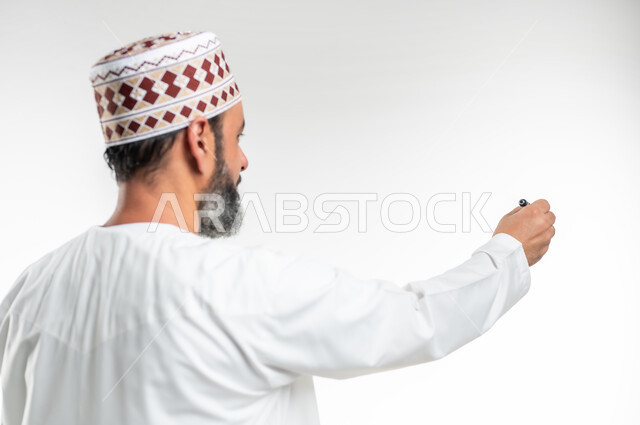 إيماءات يدين تدل على الإمساك بعنصر ما, الإستعداد للكتابة وتحديد شيء ما, بورتريه مقرب من الخلف لمعلم عربي خليجي عماني يرتدي الدشداشة و الكمه يمسك بيده قلم, مفهوم التعليم بالمناهج المقررة، خلفية بيضاء