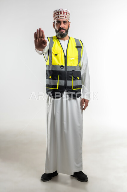 الرفض والامتناع والانزعاج, طلب التوقف وعدم الاقتراب, مفهوم الهندسة والانشاءات المعمارية، العمل في القطاع الهندسي، بورتريه لمهندس عربي خليجي عماني يرتدي الدشداشة والكمه وسترة الحماية يمد يرفع كفه نحو الأمام بإيماءات النهي, الطول الكامل للجسم، خلفية بيضاء