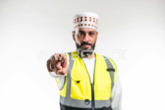 الرغبة بالإنتقام والإنزعاج، طلب التوقف عن فعل الأخطاء, مفهوم الهندسة والانشاءات المعمارية، العمل في القطاع الهندسي، بورتريه مقرب لمهندس عربي خليجي عماني يرتدي الدشداشة والكمه وسترة الحماية يرفع اصبع السبابة لتحديد شخص ما ( أنت ), خلفية بيضاء