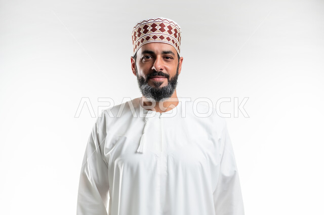 الاهتمام بالأناقة والمظهر الخارجي, التقاط الصور الشخصية للوثائق الرسمية، مفهوم الرجولة والثقة بالنفس، بورتريه مقرب لرجل عربي خليجي عماني مبتسم يرتدي الدشداشة و الكمه ينظر الى الكاميرا بإيماءات السرور والسعادة، خلفية بيضاء