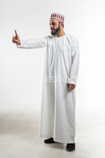 تعابير التحديد والتأكيد, اشارات تحدد هذا المكان (هنا)، الاشارة إلى شيء ما، بورتريه لرجل عربي خليجي عماني يرتدي الدشداشة والكمه يقف باستقامة و يشير بأصابع السبابة للاختيار، صورة الجسم بالطول الكامل، خلفية بيضاء