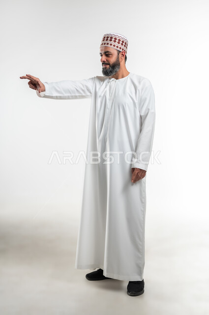 Trying to grab something, asking to stop and refrain from doing something, portrait of an Arab Gulf Omani man wearing a dishdasha and a sleeve standing straight and extending his hand with expressions that indicate this is the place (here), gestures and signs of identification and confirmation, full body length, white background
