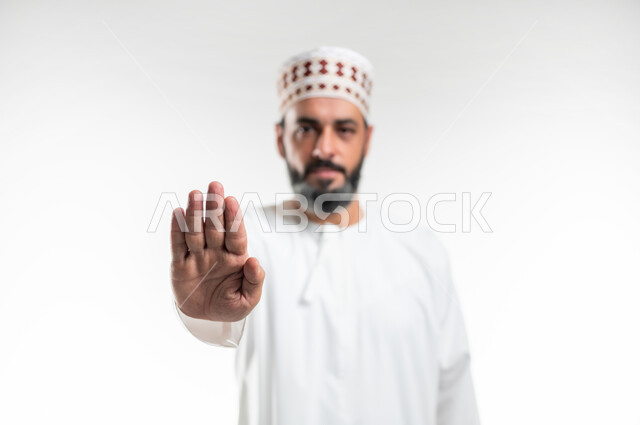 طلب التوقف وعدم الاقتراب, مفهوم الرفض والامتناع والانزعاج, بورتريه مقرب لرجل عربي خليجي عماني يرتدي الدشداشة والكمه يمد يده نحو الأمام مع رفع الكف بإيماءات النهي عن فعل امر ما, تعابير الحزم والجدية, خلفية بيضاء