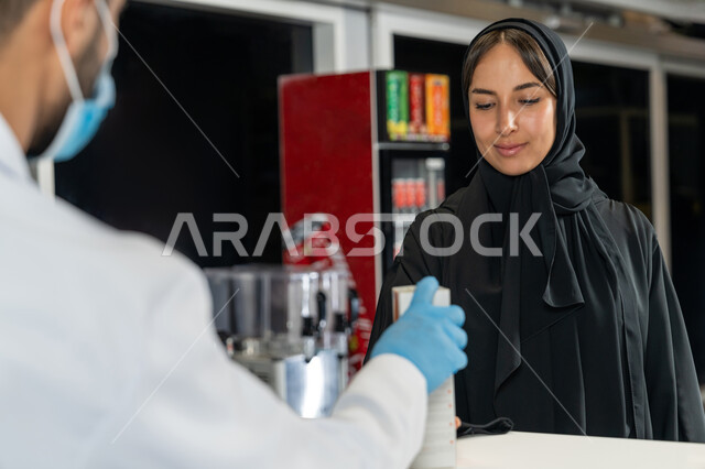بيع الادوية والمستلزمات الطبية، توفير وتجهيز الادوية اللازمة للمريضة،  إمرأة عربية خليجية إماراتية تشتري العقاقير الطبية من صيدلاني اماراتي يرتدي الكمامة الطبية للوقاية من فايروس كورونا، قراءة الروشتة الخاصة بالمريض، صرف الادوية الموجودة في الوصفات الطبية