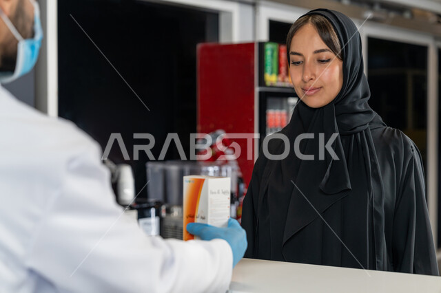بيع الادوية والمستلزمات الطبية، توفير وتجهيز الادوية اللازمة للمريضة،  إمرأة عربية خليجية إماراتية تشتري العقاقير الطبية من صيدلاني اماراتي يرتدي الكمامة الطبية للوقاية من فايروس كورونا، قراءة الروشتة الخاصة بالمريض، صرف الادوية الموجودة في الوصفات الطبية