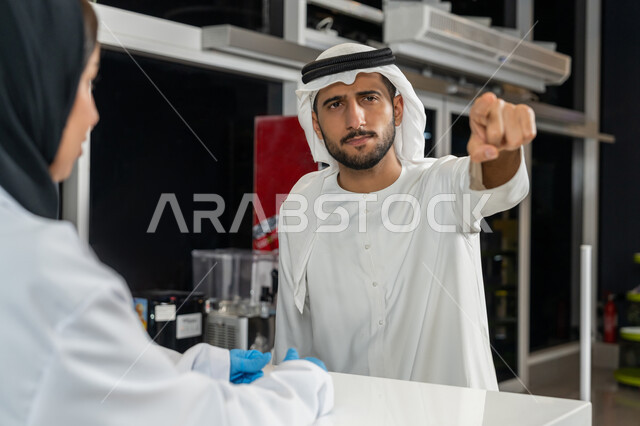 وصف الادوية المطلوبة والحالة المرضية، رجل عربي اماراتي خليجي يرتدي الغترة والكندورة يطلب من الصيدلانية بعض الأدوية يقوم بالاشارة إلى شيء ما داخل الصيدلية، بيع الادوية والمستلزمات الطبية، الاستفادة من الخدمات والرعاية الصحية