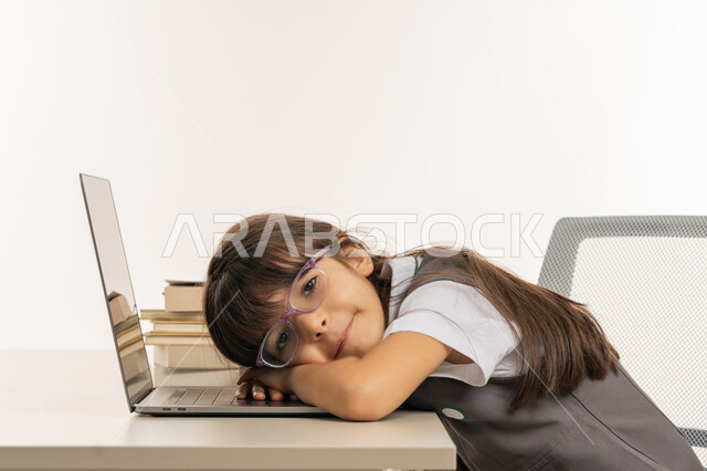 الشعور بالكسل والخمول، النوم على طاولة الدراسة، ايماءات النعاس والتعب والإرهاق، بورتريه لطالبة عربية خليجية اماراتية ترتدي اليونيفورم المدرسي تقوم بإهمال دروسها، سلبيات التعلم عن بعد، تلميذة سعودية غير محبة للدراسة، هدر وضياع الوقت، خلفية بيضاء