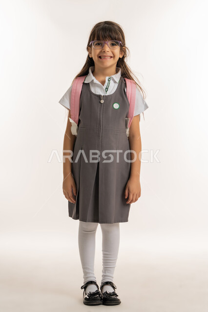 النظر الى الكاميرا إيماءات تدل على الحماس والسعادة، موسم العوده للمدارس, التهيئة والتجهيز لبداية العام الدراسي, بورتريه لطالبة عربية خليجية اماراتية ترتدي اليونيفورم الخاص وتحمل الحقيبة المدرسية, تلميذه مجتهده ومتميزه, الرغبة في طلب العلم، خلفية بيضاء.