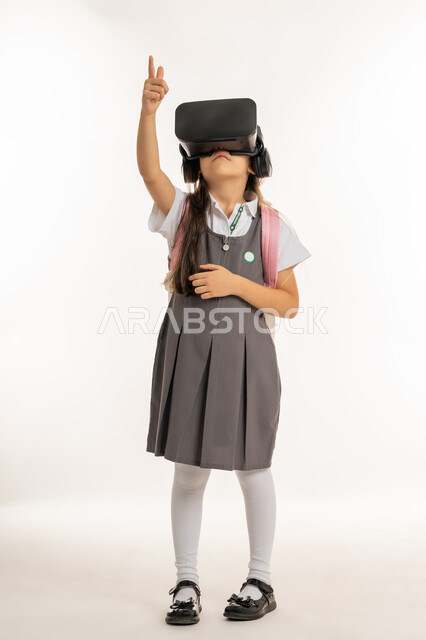 مدارس وأكاديميات متطوره، بورتريه لتلميذة عربية خليجية اماراتية ترتدي اليونيفورم والحقيبة المدرسية، طالبه مجتهدة تشير إلى شيء ما, جمع التعلم مع الترفيه بإستخدام التقنيه والتكنولوجيا الحديثه, التعليم الذكي عبر نظارات الواقع الافتراضي, خلفيه بيضاء