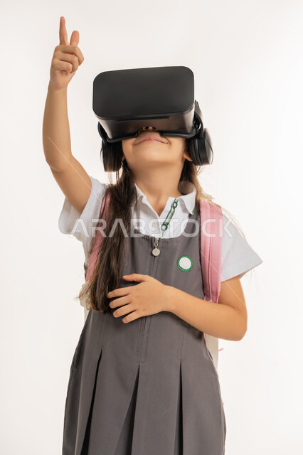 التعليم الذكي عبر نظارات الواقع الافتراضي, مدارس وأكاديميات متطوره، بورتريه لتلميذة عربية خليجية اماراتية ترتدي اليونيفورم والحقيبة المدرسية، طالبه مجتهدة تشير إلى شيء ما, جمع التعلم مع الترفيه بإستخدام التقنيه والتكنولوجيا الحديثه, خلفيه بيضاء