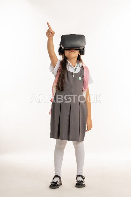 جمع التعلم مع الترفيه بإستخدام التقنيه والتكنولوجيا الحديثه, التعليم الذكي عبر نظارات الواقع الافتراضي, مدارس وأكاديميات متطوره، بورتريه لتلميذة عربية خليجية اماراتية ترتدي اليونيفورم والحقيبة المدرسية، طالبه مجتهدة تشير إلى شيء ما, خلفيه بيضاء