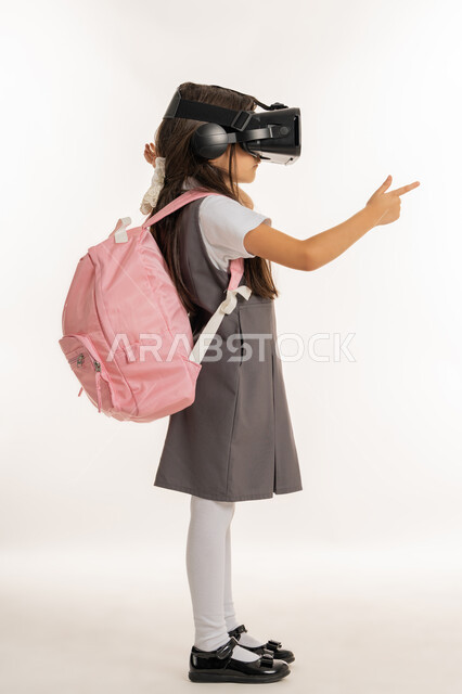 التعليم الذكي عبر نظارات الواقع الافتراضي, مدارس وأكاديميات متطوره، بورتريه من الجانب لتلميذة عربية خليجية اماراتية ترتدي اليونيفورم والحقيبة المدرسية، طالبه مجتهدة تشير إلى شيء ما, جمع التعلم مع الترفيه بإستخدام التقنيه والتكنولوجيا الحديثه, خلفيه بيضاء.
