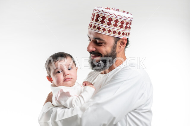 ايماءات الحب والعطف على الصغار, بورتريه مقرب لأب عربي خليجي عماني يرتدي الدشداشة ويضع الكمة يحمل ابنته الرضيعة بيديه, قضاء وقت ممتع مع الاطفال, مفهوم الاسرة السعيدة, خلفية بيضاء