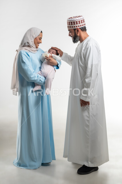 الرعايه والاهتمام بصحة ونمو الأبناء, شرب الحليب من عبوة الرضاعة، مفهوم الأمومة والرضاعة الصناعية، بورتريه لعائلة عربية خليجية عمانية مع طفلتهم، تناول الغذاء والوجبات المفيدة، قضاء أوقات ممتعه مع الأطفال, صورة الجسم بالطول الكامل, خلفية بيضاء