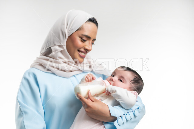 الرعايه والاهتمام بصحة ونمو الأبناء, شرب الحليب من عبوة الرضاعة، مفهوم الأمومة والرضاعة الصناعية، بورتريه مقرب لأم عربية خليجية عمانية مبتسمة تحمل طفتلها الصغيرة، تناول الغذاء والوجبات المفيدة، والدة سعودية تقوم بقضاء أوقات ممتعه مع الأطفال, خلفية بيضاء