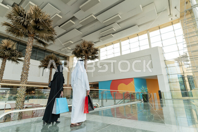 قضاء وقت ممتع في إحدى المولات التجارية، المشاركة في اختيارات التسوق وتبادل الآراء، زوجين عربيين خليجيين اماراتيين يتجولان في المول ويحملان الأكياس الورقية الملونة، الإستفادة من العروض والتخفيضات الموسمية، الاستمتاع بالشراء والتبضع، إقتناء المستلزمات اللازمة